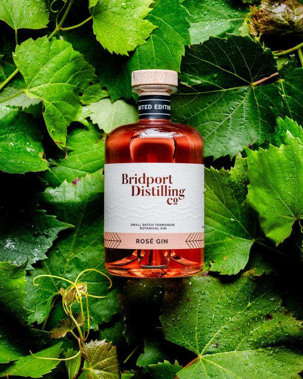 Bottle of Bridport Distilling Co's limited edition Rosé gin laying on a bed of green grape vines