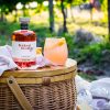 Bottle of Bridport Distilling Co's limited edition Rosé Gin sat in a picnic setting with a cocktail made from the gin with vineyard as the background setting